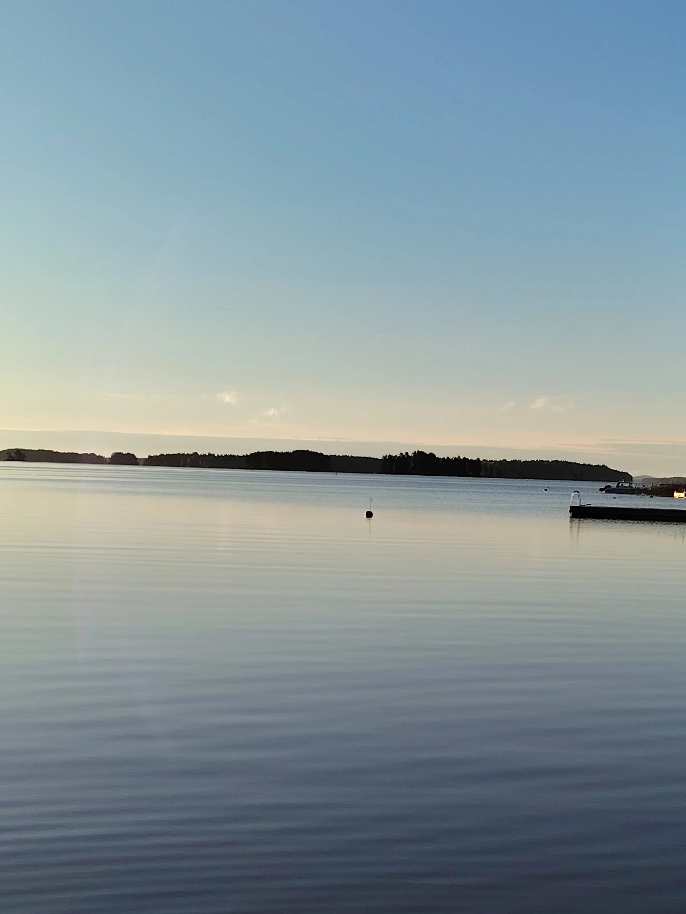 A still lake in the early morning, a forested shoreline on the horizon and a pier on the right.